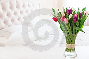 Home interior with pink tulips in a vase on a light bedroom background