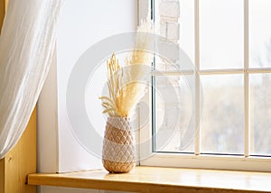 Home interior. Reed plume stem, vase with dry flower on window