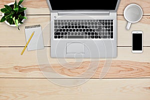 Home interior. Top view of wooden desk with laptop, cell phone, blank notebook for text and pencil, empty white mug and green flow
