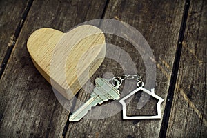 Home key with house keychain and wooden heart mock up on vintage wood background, home sweet home concept