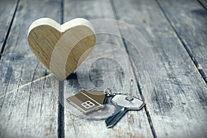 Home key with house keychain and wooden heart mock up on vintage wood background, home sweet home concept