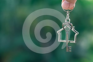 Home key with house keyring hanging with green garden background