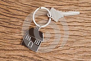 Home key with house keyring or keychain on wooden table using as home ownership, mortgage or buy and sell property and real estate