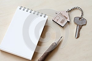 Home key with house keyring, pencil, note book on wooden table