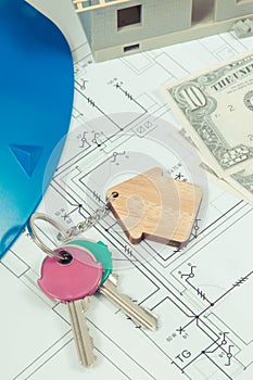 Home keys, currencies dollar, electrical construction diagrams and small house under contruction. Building or buying home