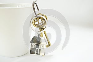 Home keys with house keyring hanging on white coffee cup