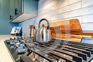 Home kitchen interior with kettle over the burner of a cooktop with five knobs