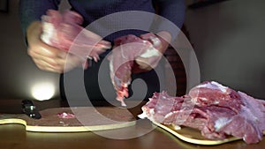 Home kitchen. A man is shifting pieces of pork meat from one cutting board to another.