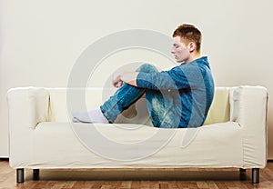 Young pensive man sitting on couch