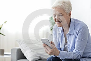 Home leisure for seniors. Happy elderly woman using smartphone at home