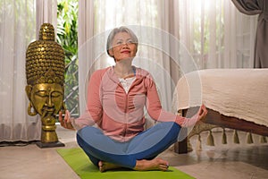 Home lifestyle - beautiful and happy mature woman with gray hair on her 50s doing yoga and meditation exercise at Asian deco