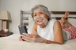 Home lifestyle portrait of attractive and happy middle aged woman on her 50s using internet mobile phone in bed relaxed and