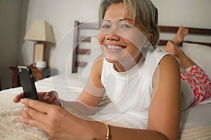 Home lifestyle portrait of attractive and happy middle aged woman on her 50s using internet mobile phone in bed relaxed and