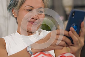 Home lifestyle portrait of attractive and happy middle aged woman on her 50s using internet mobile phone at living room couch