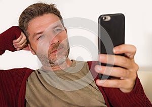 Home lifestyle portrait of attractive and relaxed unshaven man 30s or 40s  lying on couch using internet on mobile phone enjoying