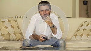 Home lifestyle portrait of young attractive and happy man watching television show or movie holding TV remote controller enjoying