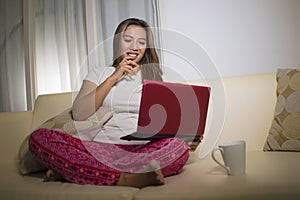 Home lifestyle portrait of young attractive and natural Asian Indonesian woman in pajamas pants relaxed on couch networking using