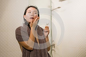 Young beautiful and happy Asian Chinese woman applying serum facial skin care and face treatment in the bathroom enjoying morning photo