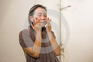 Young beautiful and happy Asian Korean woman applying serum facial skin care and face treatment in the bathroom enjoying morning photo