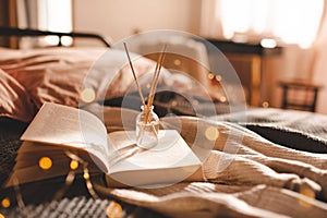 Home liquid fragrance in glass bottle with bamboo sticks on paper book in bed over glow lights close up.