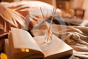 Home liquid fragrance in glass bottle with bamboo sticks on paper book in bed over glow lights close up.