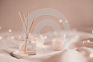 Home liquid fragrance in glass bottle and burning candles staying on white ceramic tray in bed close up.