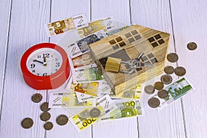 Home loan concept. Wooden house, red alarm clock, house keys, euro bills
