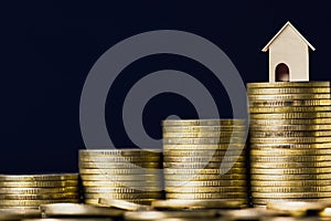 Home loan, mortgages, debt, savings money for home buying concept. A small house model on rising stack of coins with black