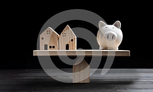 Home loans market. Model house and piggy bank balancing on a seesaw photo