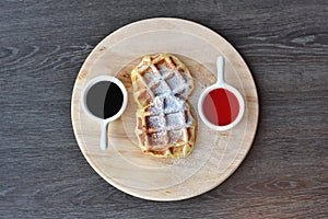 Home made Belgian waffles served with strawberry sauce and chocolate sauce over a wooden  board