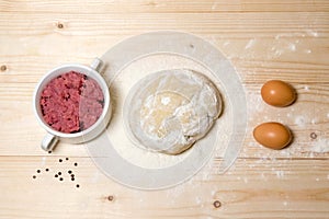 Home-made dough, prepared meat, eggs, flour on a wooden background. Products for cooking dumplings, dumplings with meat. Home