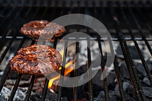 Home-made juicy beef burgers grilled on the barbecue. Fire from the charcoal beneath the hamburger. photo