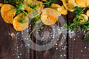 Home made potato chips with parsley on dark rustic wooden background. Tasty food. Top view. Flat lay. Copy space