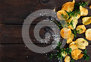 Home made potato chips with parsley on dark rustic wooden background. Tasty food. Top view. Flat lay. Copy space