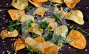 Home made potato chips with parsley on dark rustic wooden background. Tasty food. Top view. Flat lay. Copy space