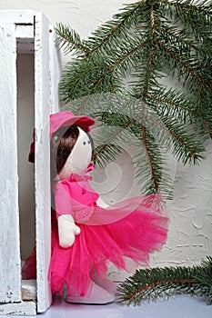 Home-made rag doll in pink clothes. Against the background of a fir branch and a white wooden box