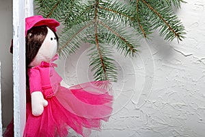 Home-made rag doll in pink clothes. Against the background of a fir branch and a white wooden box