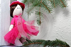 Home-made rag doll in pink clothes. Against the background of a fir branch and a white wooden box