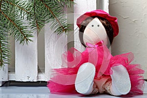 Home-made rag doll in pink clothes. Against the background of a fir branch and a white wooden box