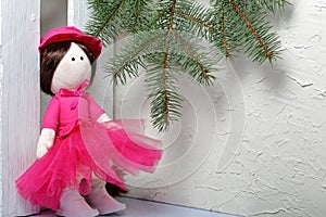 Home-made rag doll in pink clothes. Against the background of a fir branch and a white wooden box