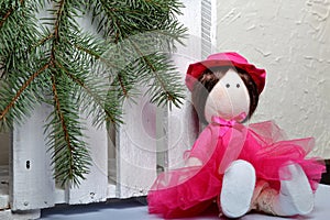 Home-made rag doll in pink clothes. Against the background of a fir branch and a white wooden box