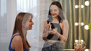 Home make-up artist services. A girl does a make-up on her friend while standing near a mirror in a cozy home