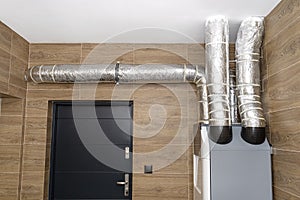 Home mechanical ventilation with heat recovery hanging on the wall in a modern gas boiler room with brown ceramic tiles imitating