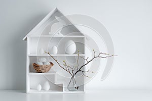 Home minimalist interior with Easter decor. Branches with budding buds in a glass vase on shelves in the shape of a