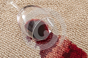 Home mishap and domestic accident concept with close up of  a spilled glass of red wine on brown carpet