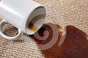 Home mishap, stained carpet, and domestic accident concept with close up of a spilled cup of coffee leaving a stain on the brown photo