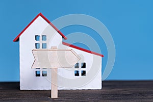 Home model with wooden signboard. Buying house concept. Blue background, front view