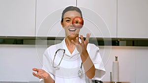 Home nurse throwing and catching apple and smiling in kitchen