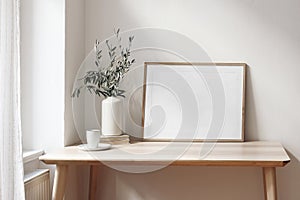 Home office concept. Empty horizontal wooden picture frame mockup. Cup of coffee on wooden table. White wall background