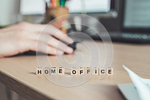 Home office concept: â€œHome Officeâ€ letters in foreground, man working in home office in blurry background